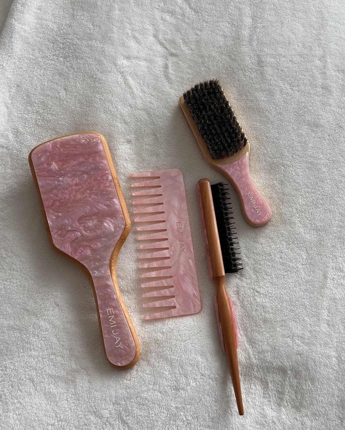Escova para cabelo cacheado e pente marmorizados rosa com madeira sobre tecido branco macio;