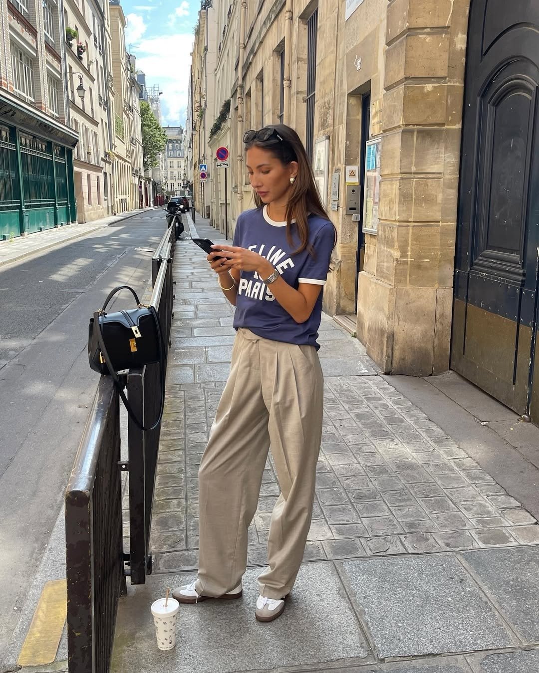 Look com calça pantalona bege de tecido leve combinada a camiseta azul com detalhes brancos, modelo posa casual e