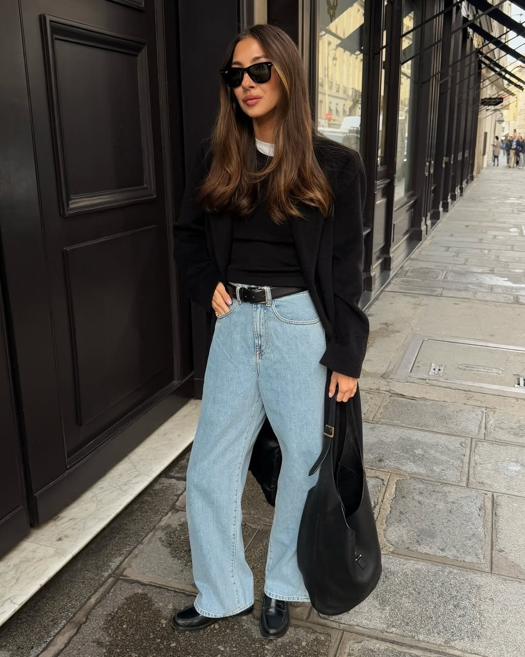 Mocassim feminino com calça jeans wide leg; modelo posa de blazer preto, bolsa maxi e óculos escuros e mocassim.