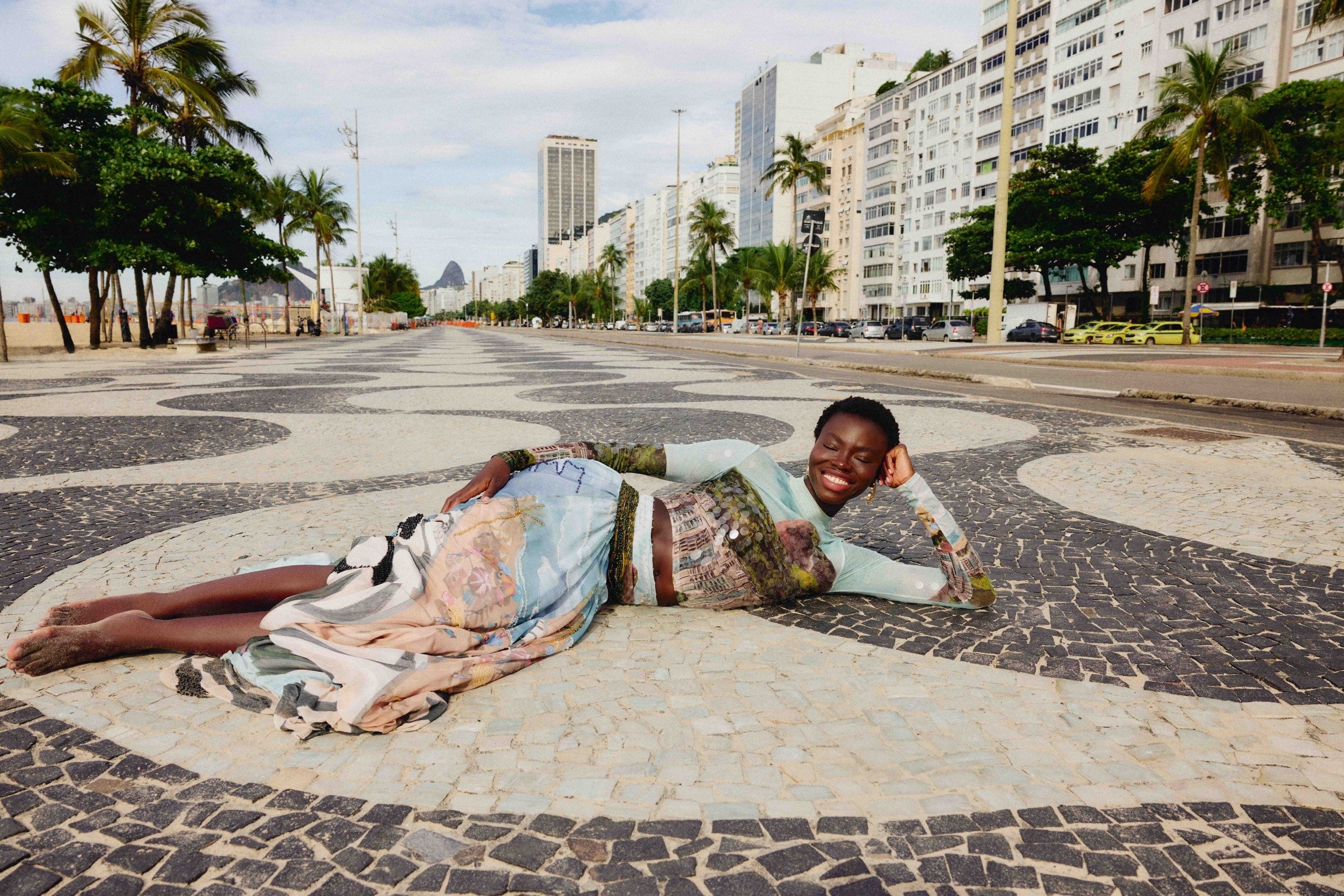 Campanha Farm com modelo deitada na calçada de mosaico carioca, usando blusa manga longa e saia fluida em tons pastel e
