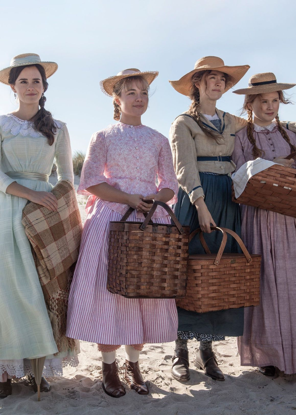 Quatro mulheres em vestidos longos de algodão com rendas e estampas delicadas, chapéus de palha e cestos de piquenique.