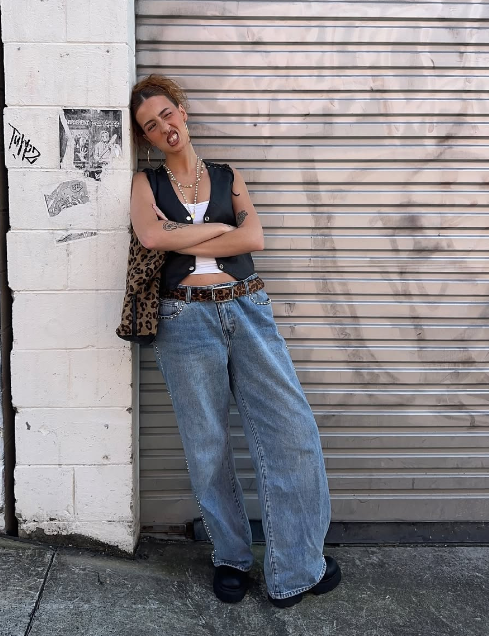 Looks de última hora para festivais: modelo posa de colete preto, jeans amplo e oncinha com atitude urbana.