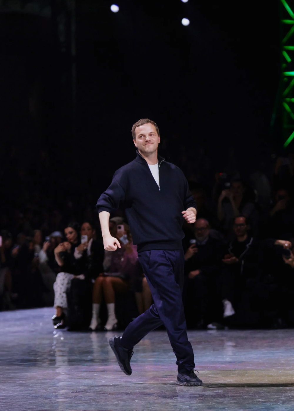 Chanel em clima confiante: homem caminha na passarela com malha azul-marinho, calça reta e tênis escuros diante do público.