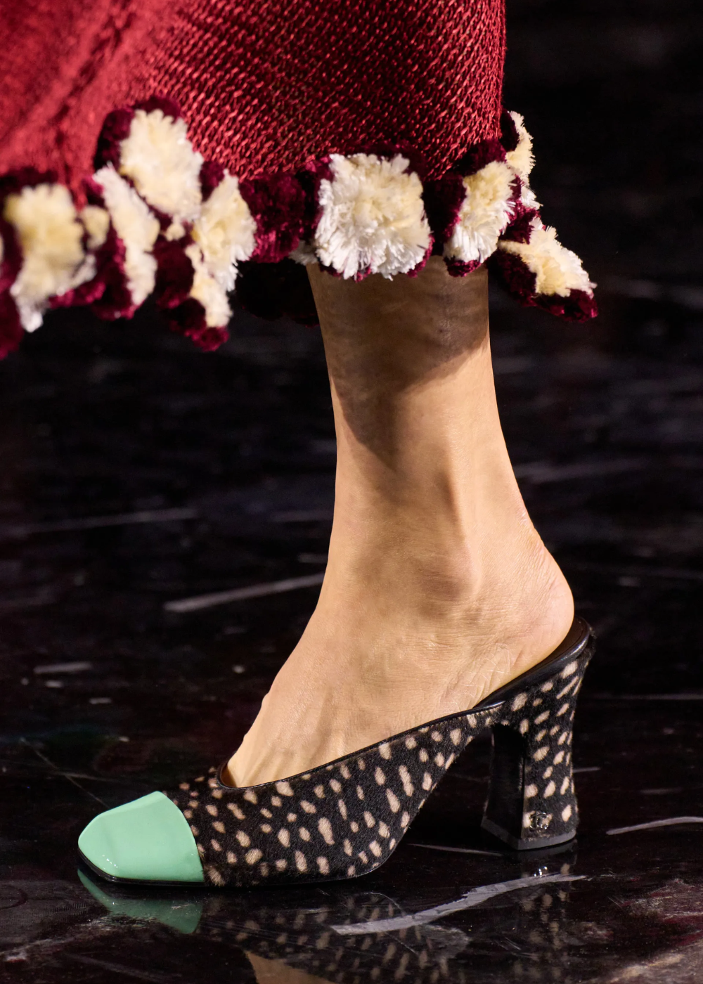 Chanel destaca mule de salto bloco preto com estampa orgânica e biqueira verde, sob barra vinho com pompons.