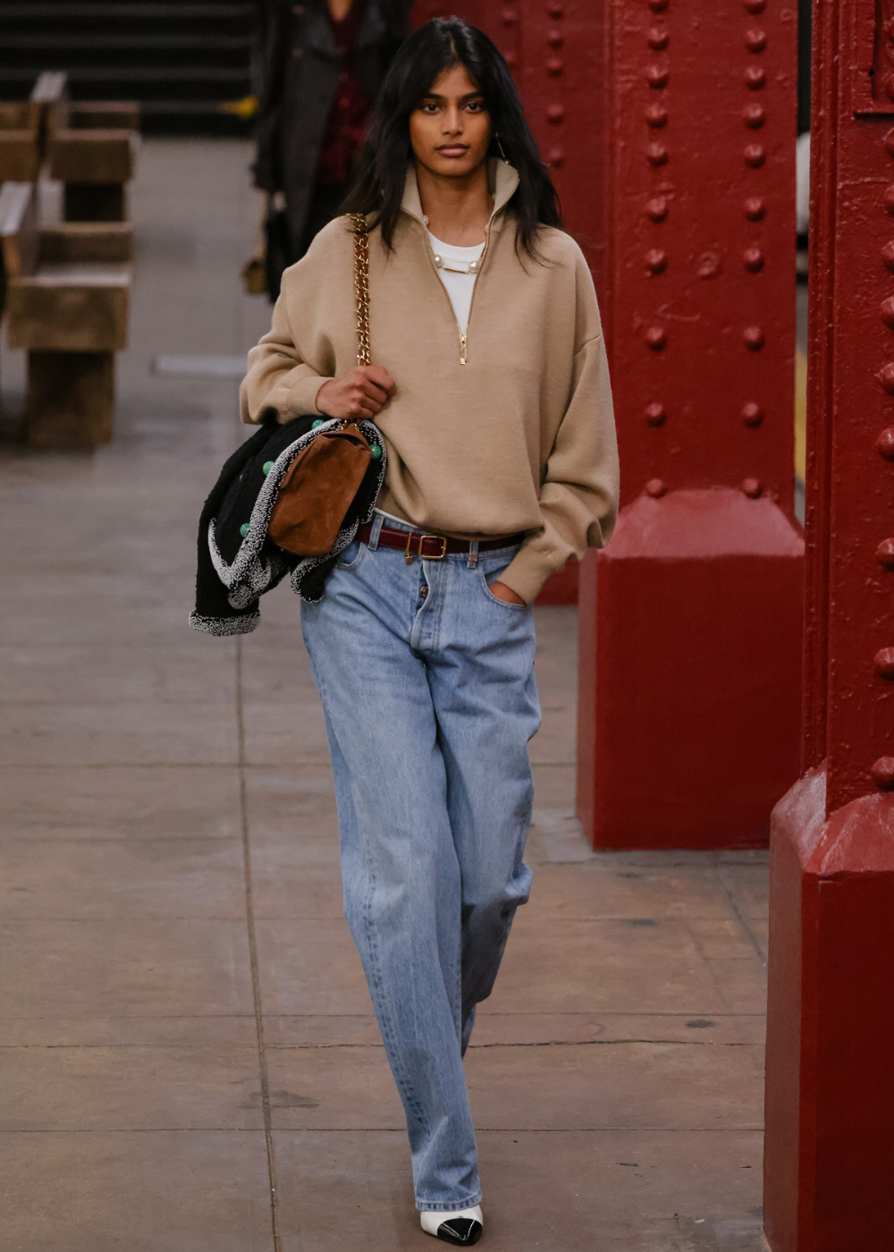 Chanel: modelo caminha com moletom bege amplo, jeans claro e bolsa de corrente dourada em clima urbano elegante.