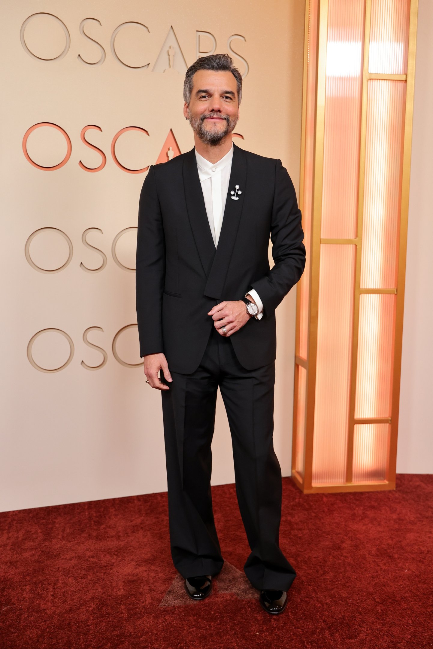 Brasileiros no Oscar: homem posa de terno preto de alfaiataria e camisa branca no tapete vermelho. Texto: OSCARS