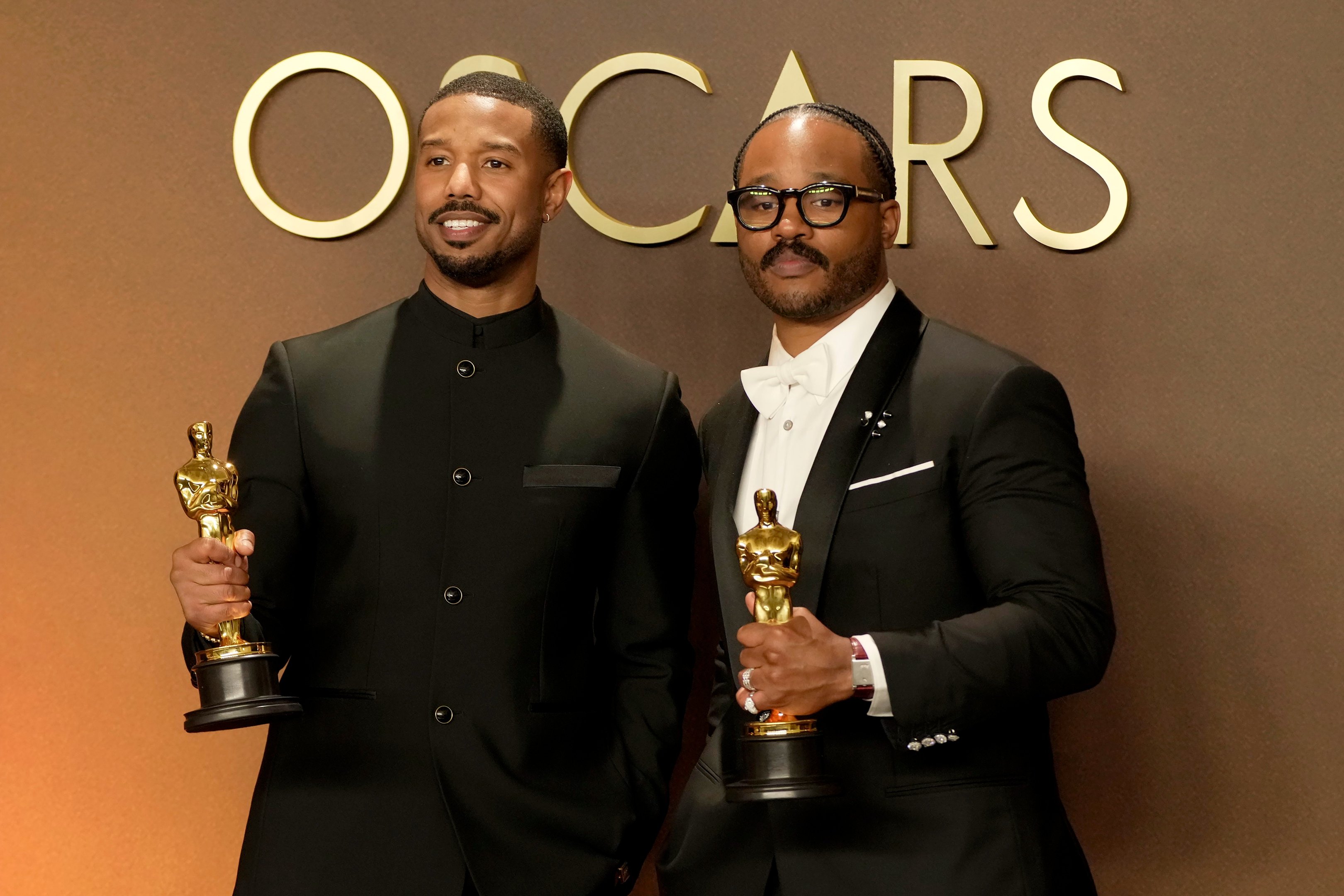 Sinners: homens posam com alfaiataria preta e estatuetas douradas diante de fundo marrom elegante. Texto: OSCARS