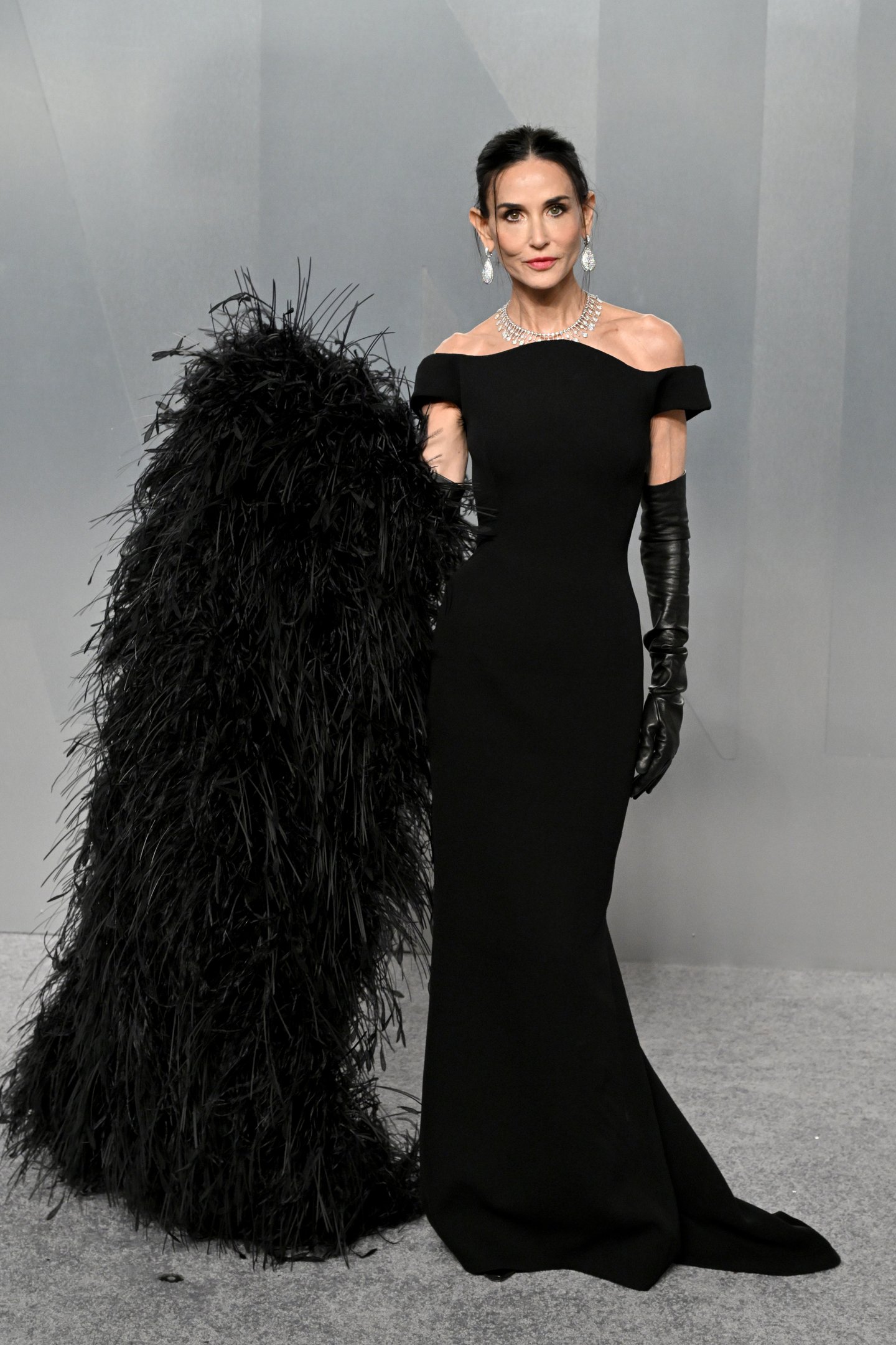 After party do Oscar 2026: atriz posa com vestido preto ombro a ombro, luvas longas e plumas, em clima sofisticado.