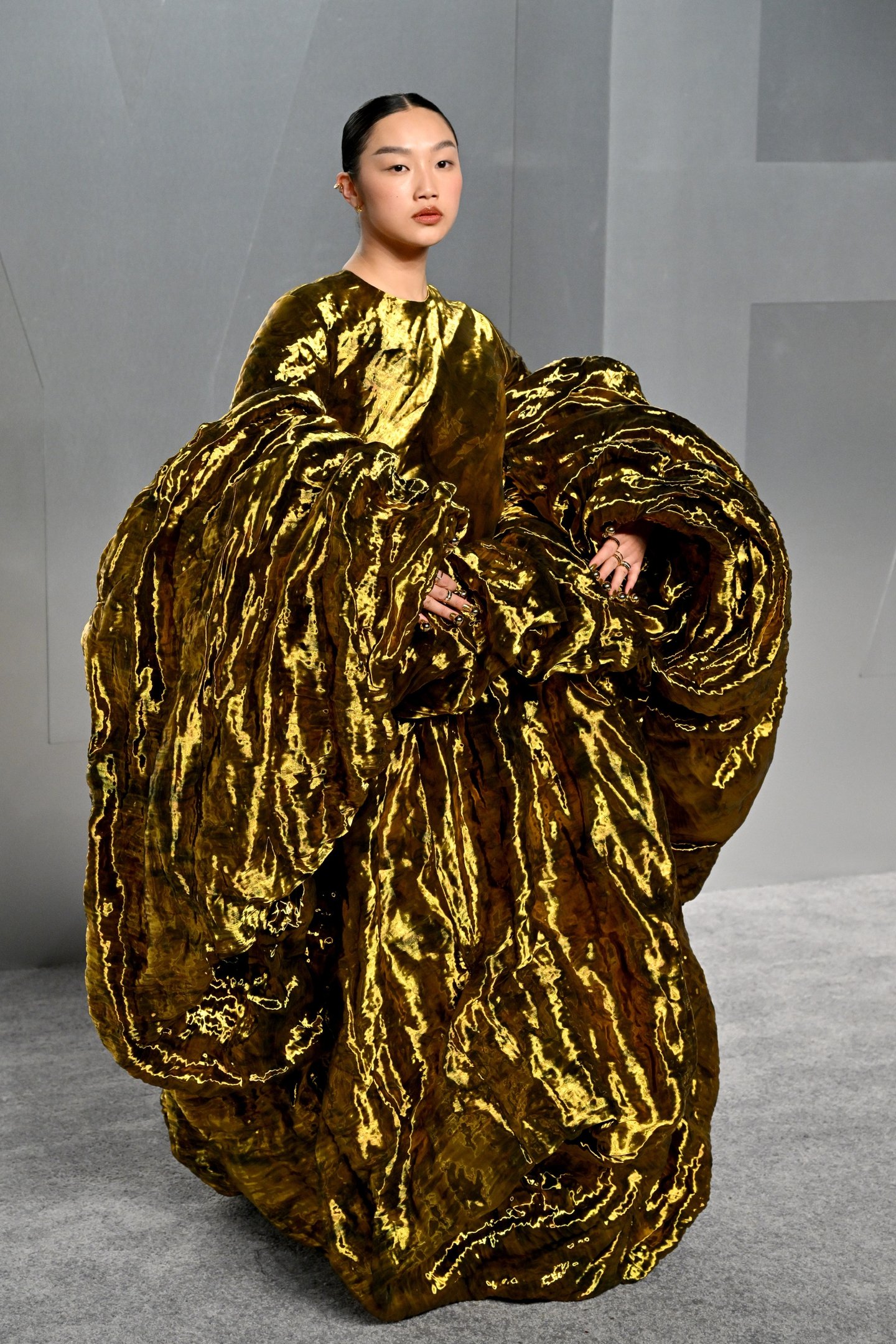 After party do Oscar 2026: modelo posa com vestido dourado metálico escultural e volumoso em clima dramático sofisticado