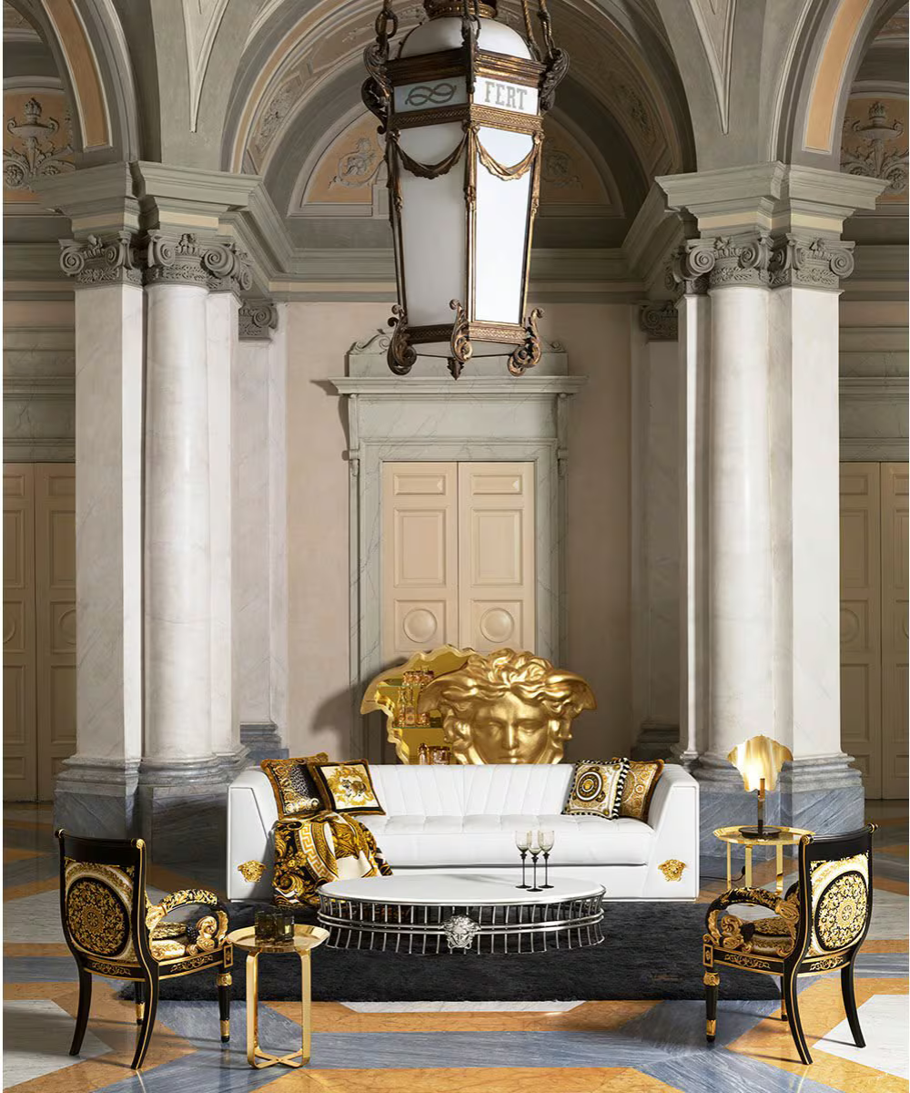 Sala luxuosa Versace com sofá branco de couro, almofadas e poltronas pretas com dourado, mesa oval e detalhes em ouro, em