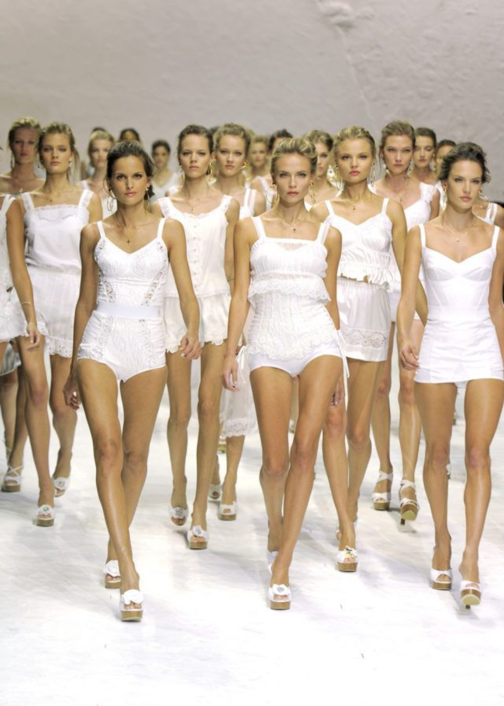 Modelos caminham com postura confiante em desfile da indústria da moda usando peças brancas delicadas.