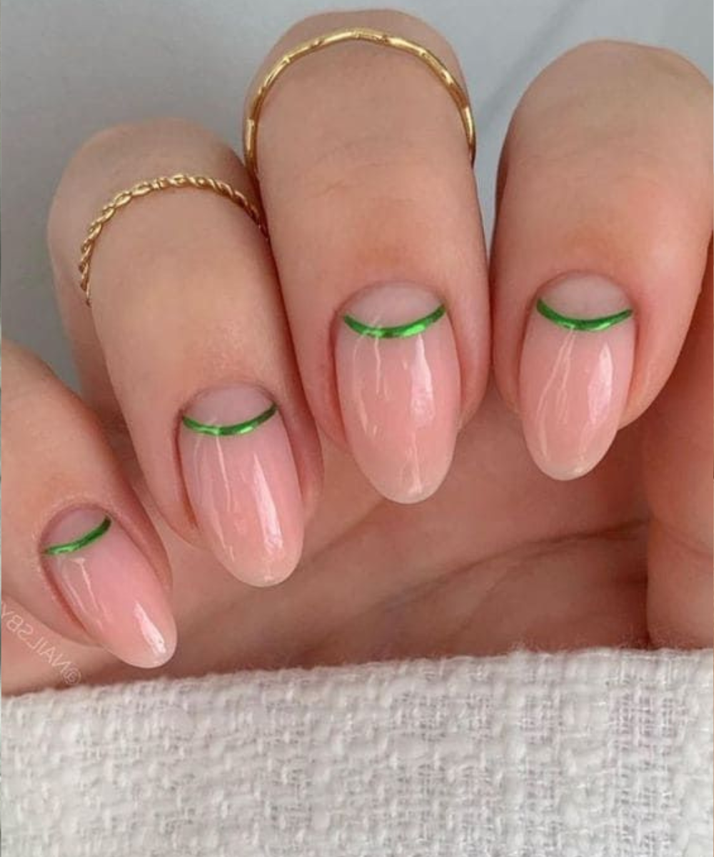 Esmaltação polêmica com base nude glossy e linha metálica verde neon na raiz das unhas ovais, destacando delicadeza e
