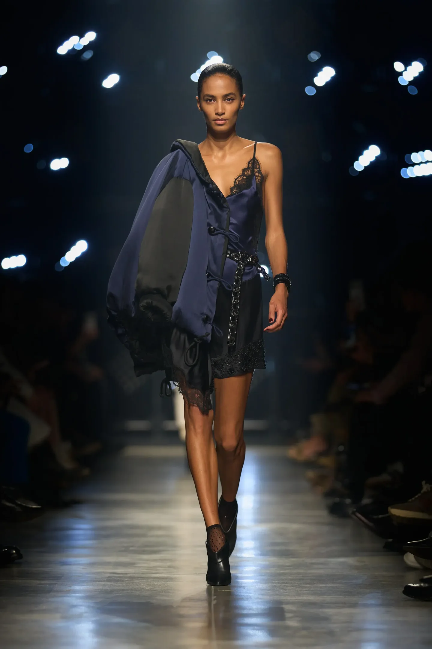 Modelo Isabel Marant caminha com vestido slip dress azul marinho de cetim e renda, jaqueta oversized preta e acessórios