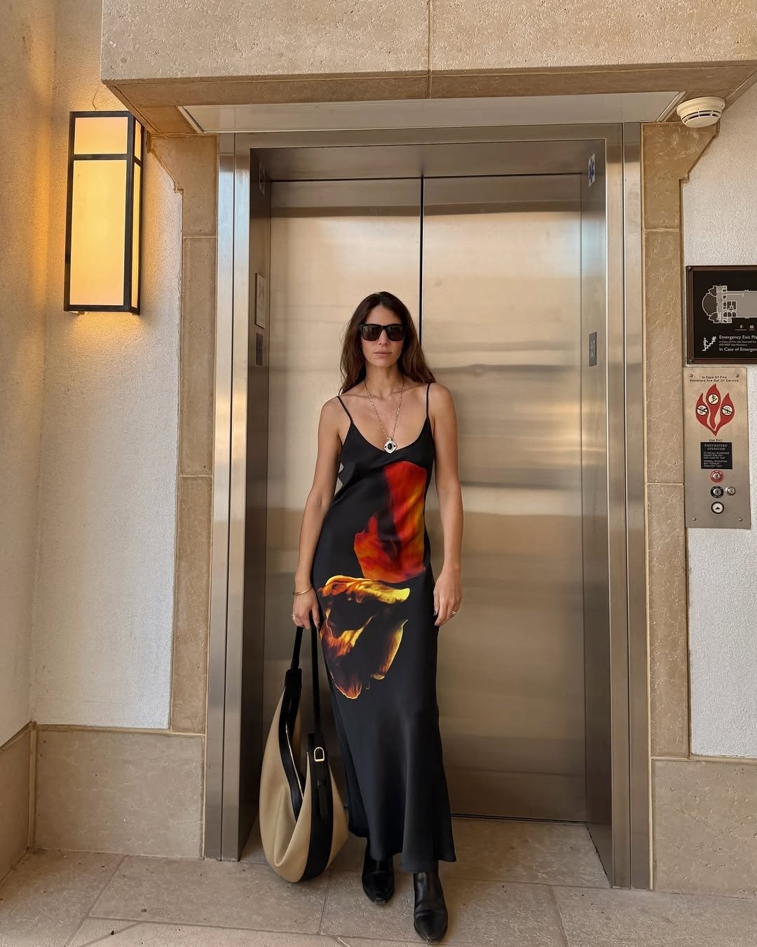 Modelo posa com vestidos tendência 2026 em cetim preto longo com estampa abstrata em tons quentes, complementado por bolsa