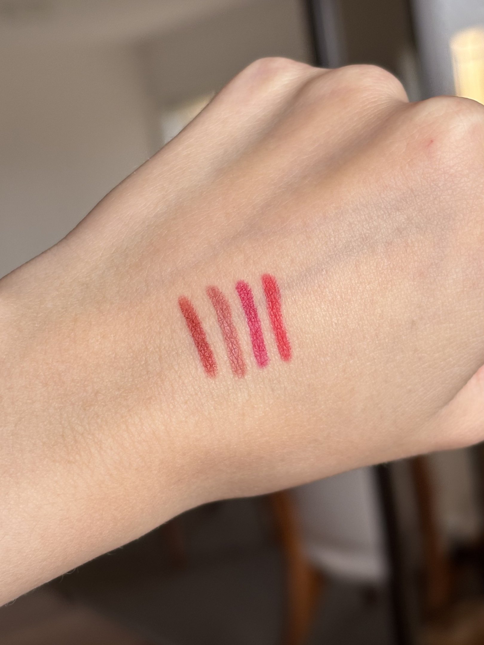 Lápis labial da Nars em swatches na mão, com quatro tons rosados e avermelhados de acabamento macio sob luz natural