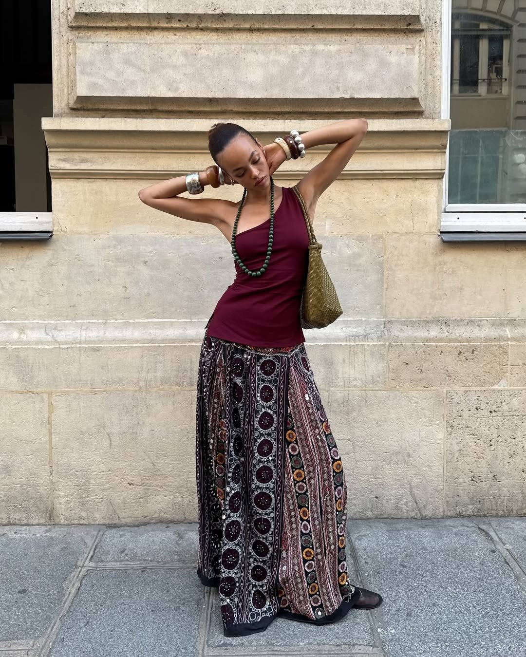 Look de festival: modelo posa com blusa vinho assimétrica, saia estampada fluida e acessórios boho em clima leve.