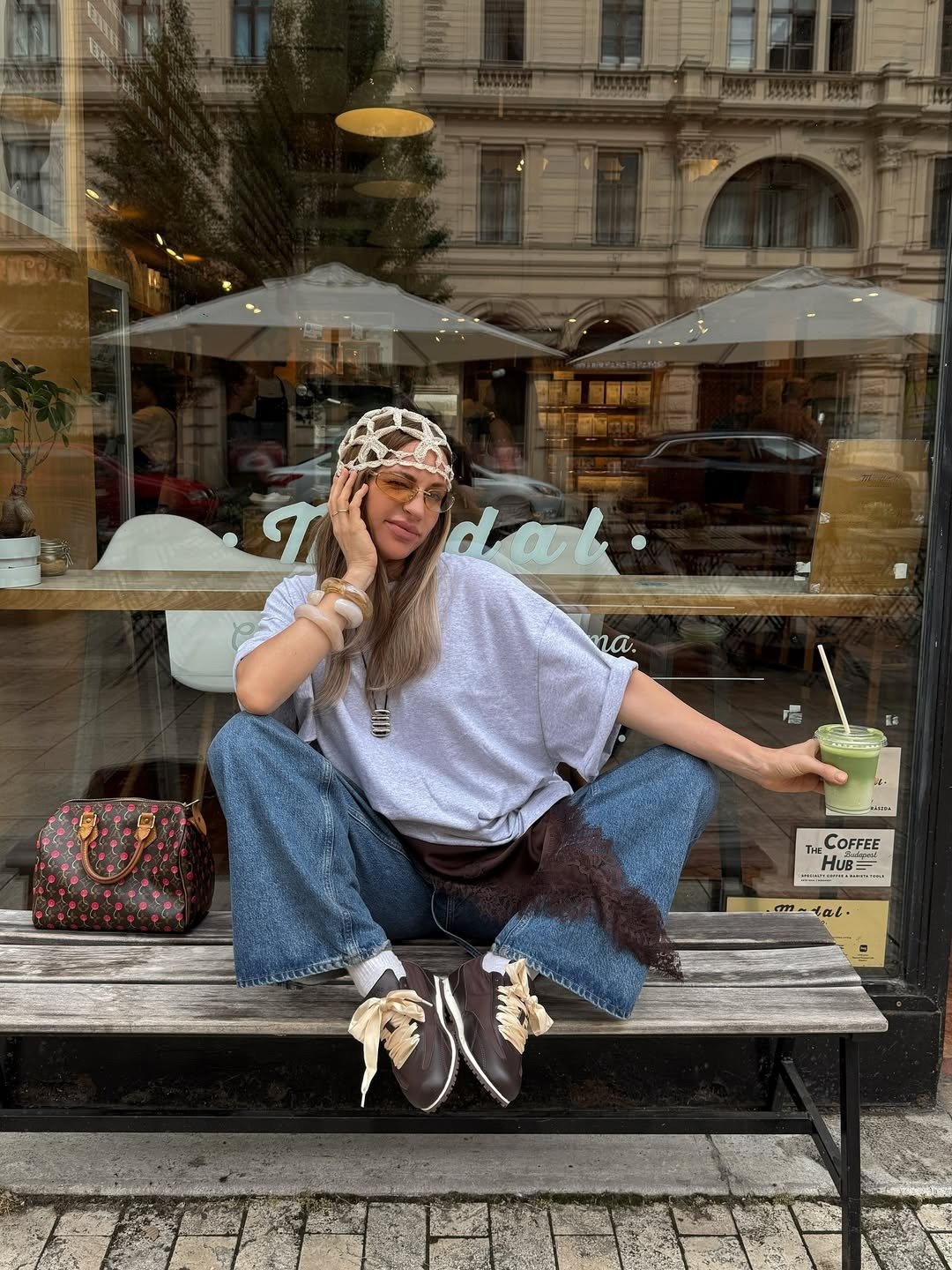 Look de festival com modelo sentada, camiseta ampla lilás, jeans azul, lenço rendado e tênis marrom com laços, clima