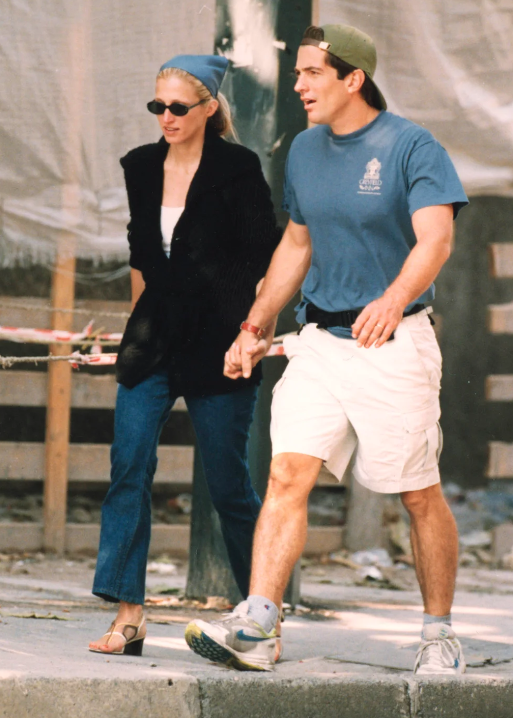 Carolyn Bessette exibe looks da década de 90 com blazer preto oversized, jeans reto, sandália de tiras e lenço azul, em