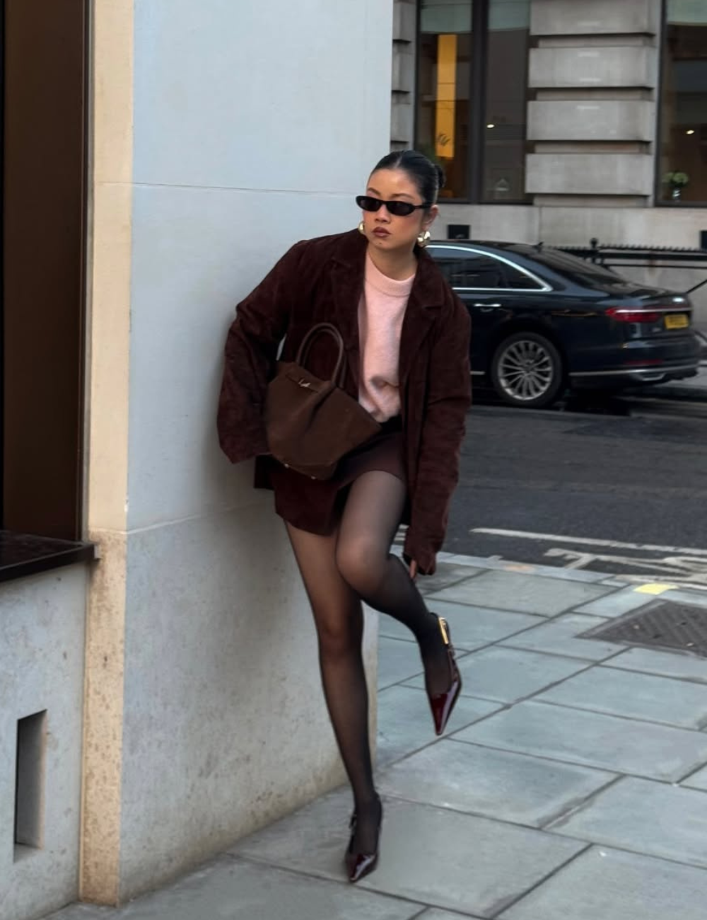 Looks com meia-calça: modelo posa na calçada com blazer vinho, malha rosa, bolsa marrom e atitude sofisticada.