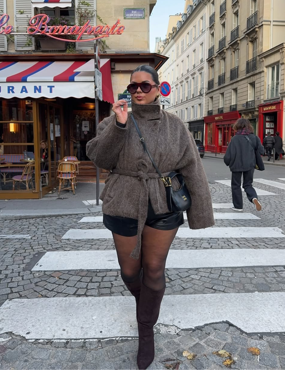 Looks com meia-calça: modelo posa na faixa com casaco marrom felpudo, short preto e bota over the knee.