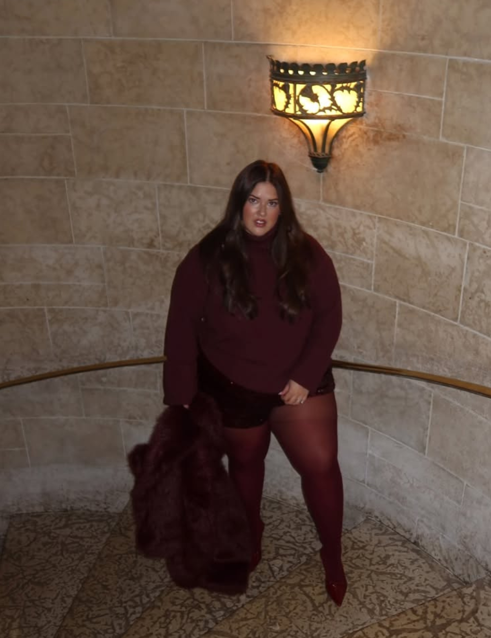 Looks com meia-calça: modelo posa em tricô e shorts vinho, com casaco felpudo, em escada de pedra com luz quente.