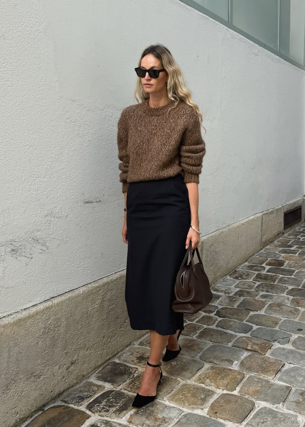 Modelo caminha com postura confiante usando look com saia lápis preta de tecido estruturado e suéter marrom de tricô.