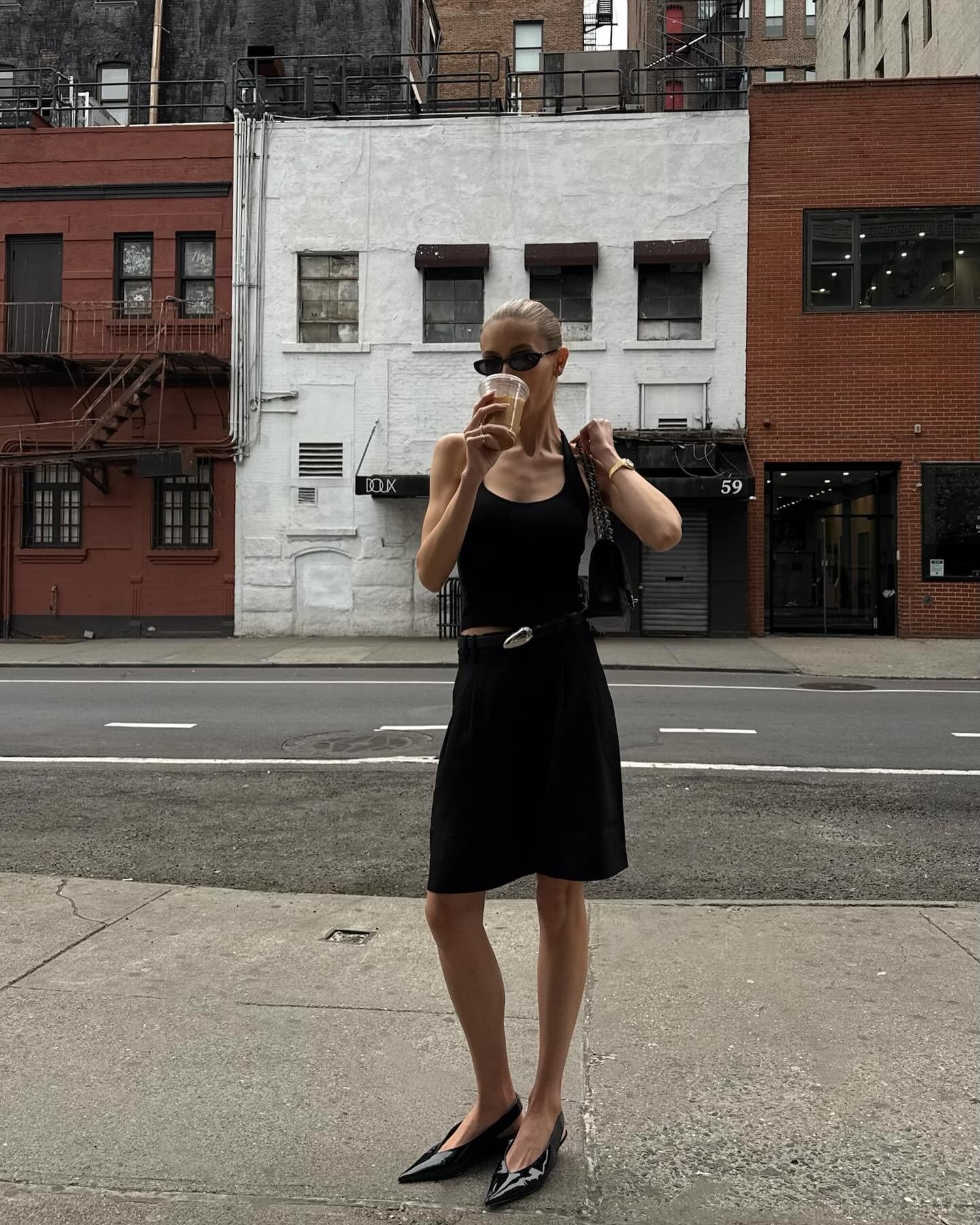 Looks criativos: modelo posa de preto minimalista com óculos e sapatilha em rua urbana. Texto: DOLX 59