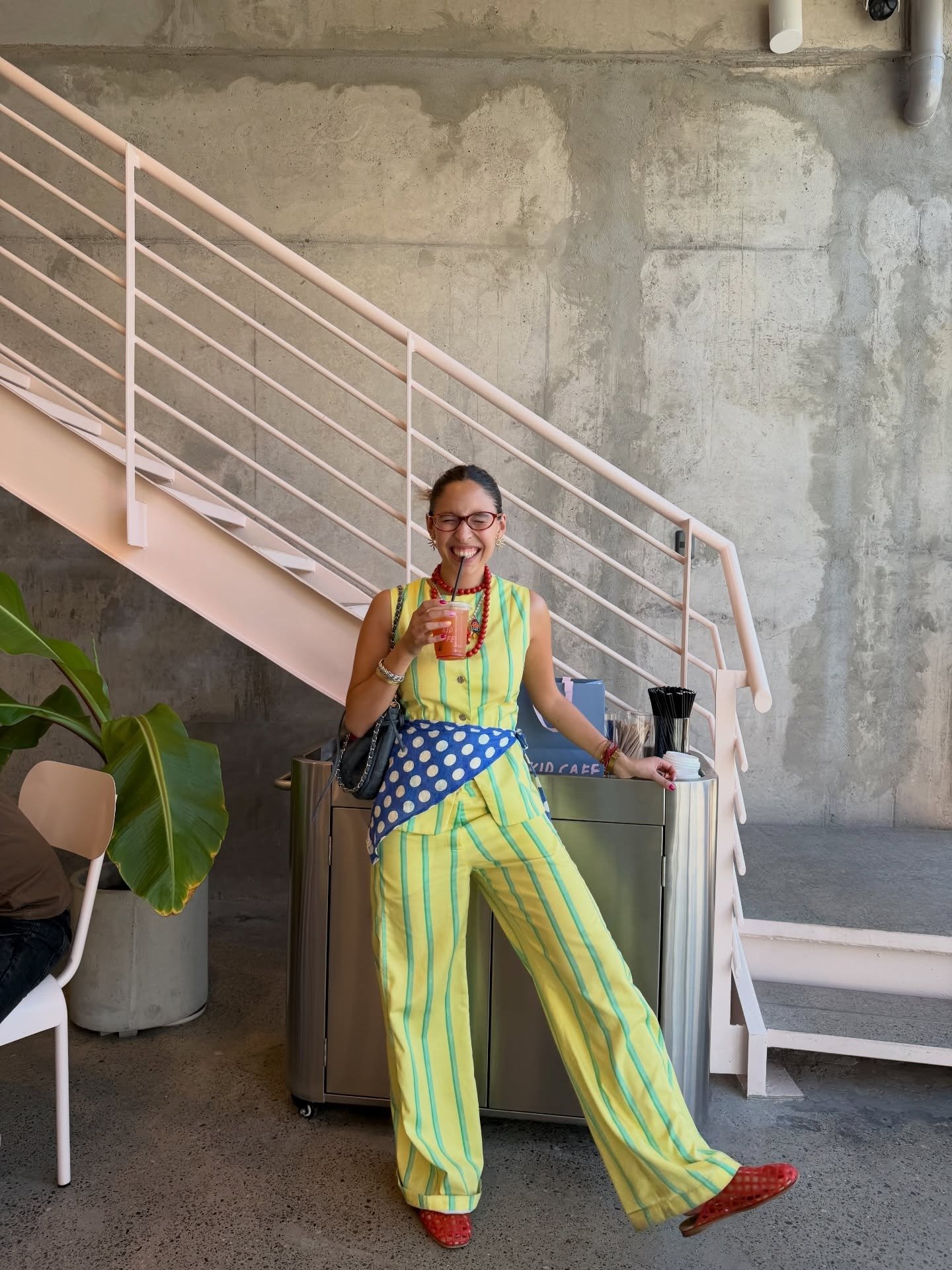 Looks criativos: modelo posa sorrindo com conjunto listrado amarelo, lenço poá azul e clima leve em café industrial.