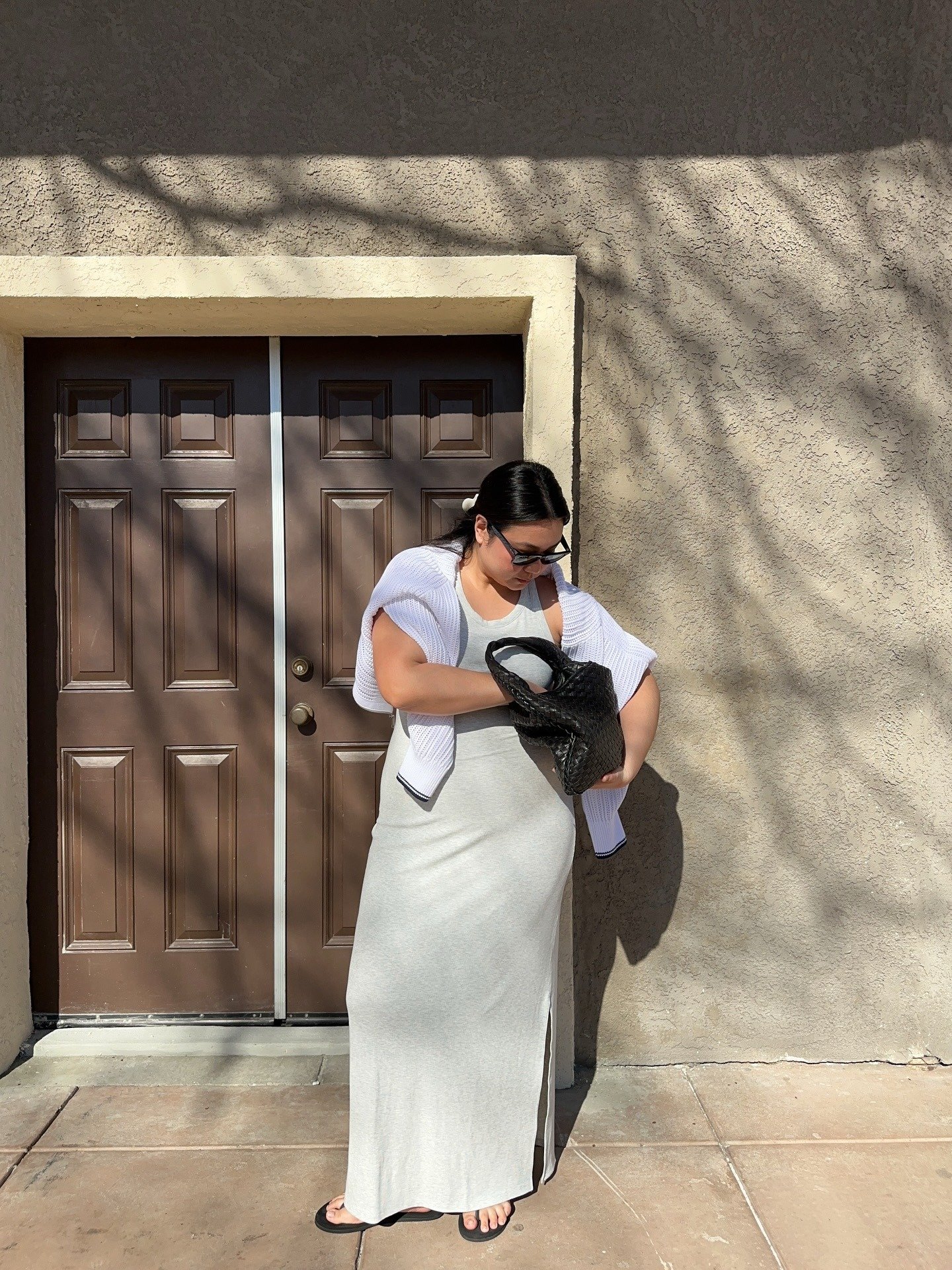 Looks criativos com modelo posa de vestido canelado cinza, tricô branco e bolsa preta sob luz suave e clima casual.