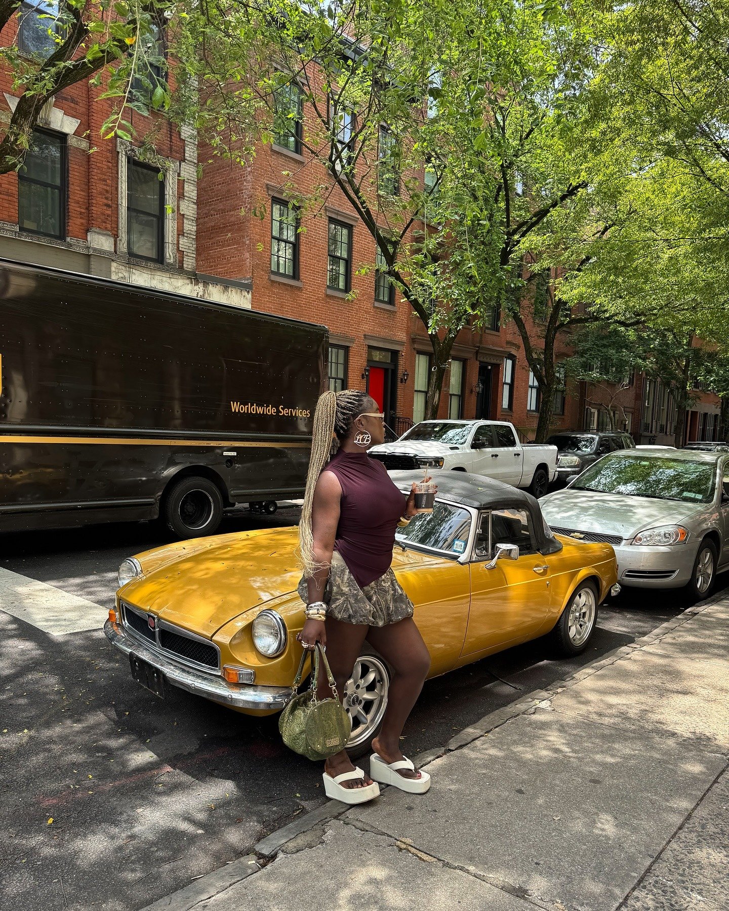 Looks criativos: modelo posa com blusa vinho e minissaia estampada ao lado de conversível amarelo.