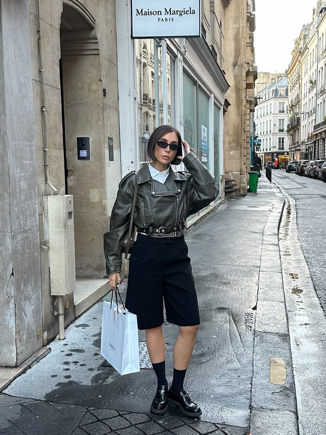 Look para faculdade com jaqueta biker cropped de couro verde, bermuda preta de alfaiataria, camisa branca, meias pretas