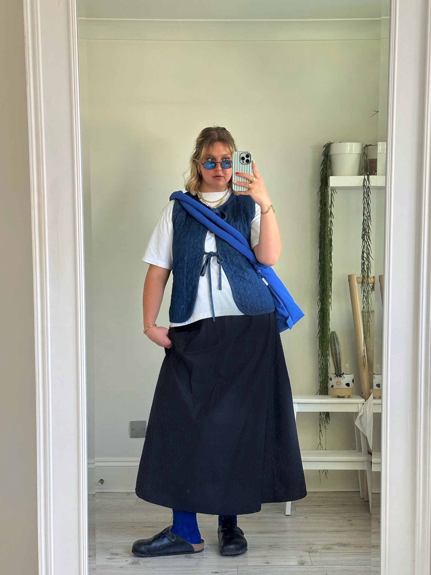 Looks para faculdade com saia preta longa, camiseta branca oversized, colete azul texturizado, bolsa azul vibrante