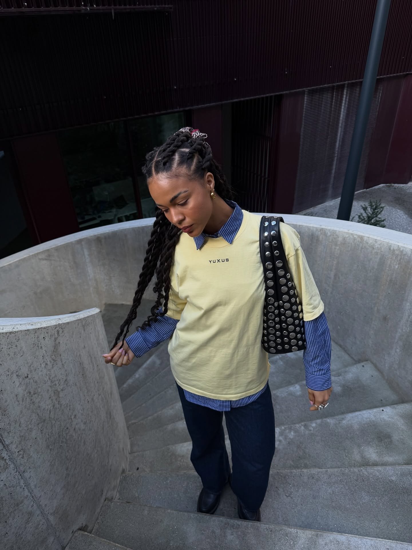 Look para faculdade com camiseta amarela sobre camisa azul listrada, jeans escuro e bolsa preta de tachas, modelo desce