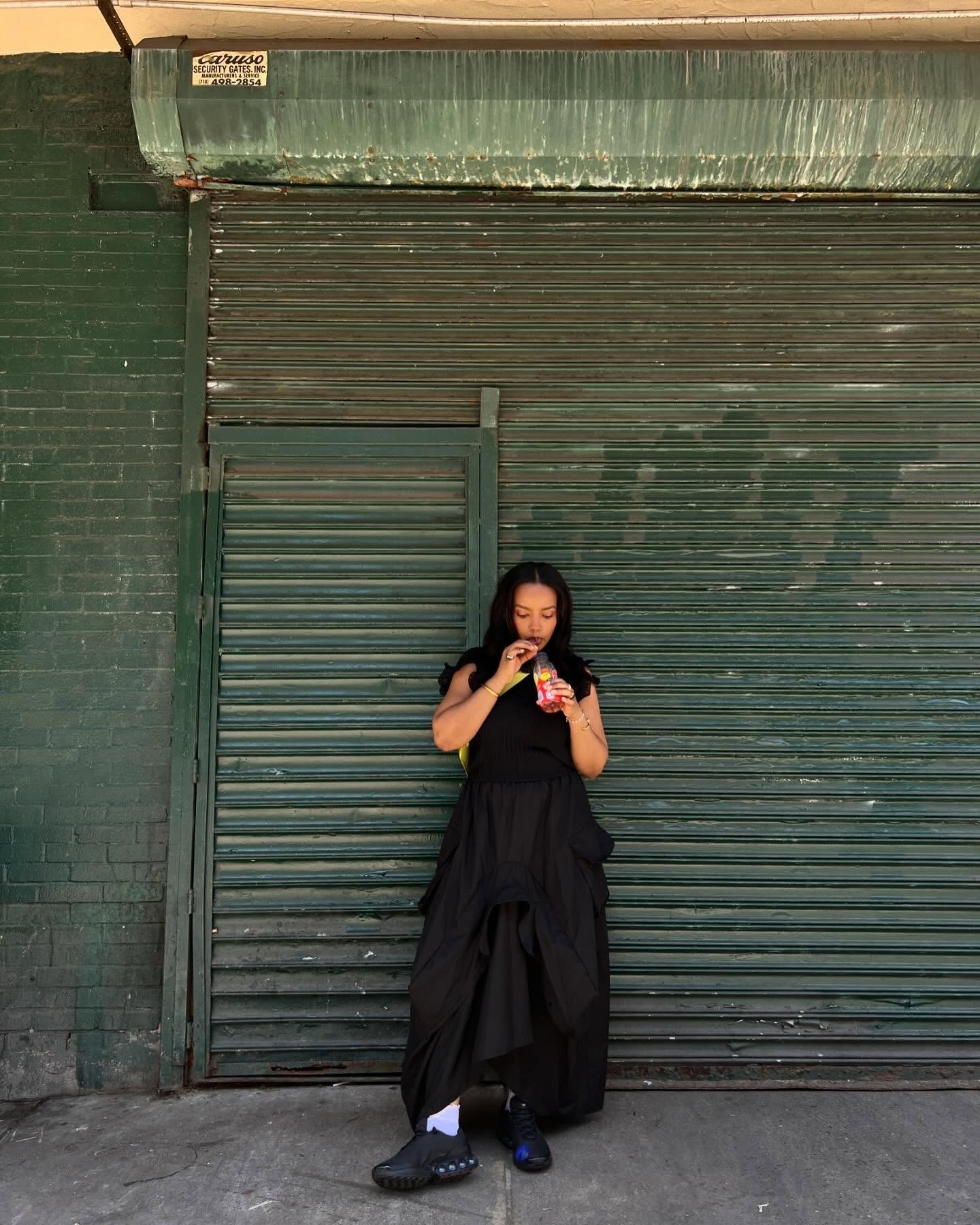 Look para faculdade com vestido preto longo de tecido leve e modelagem fluida, tênis esportivo e mochila amarela