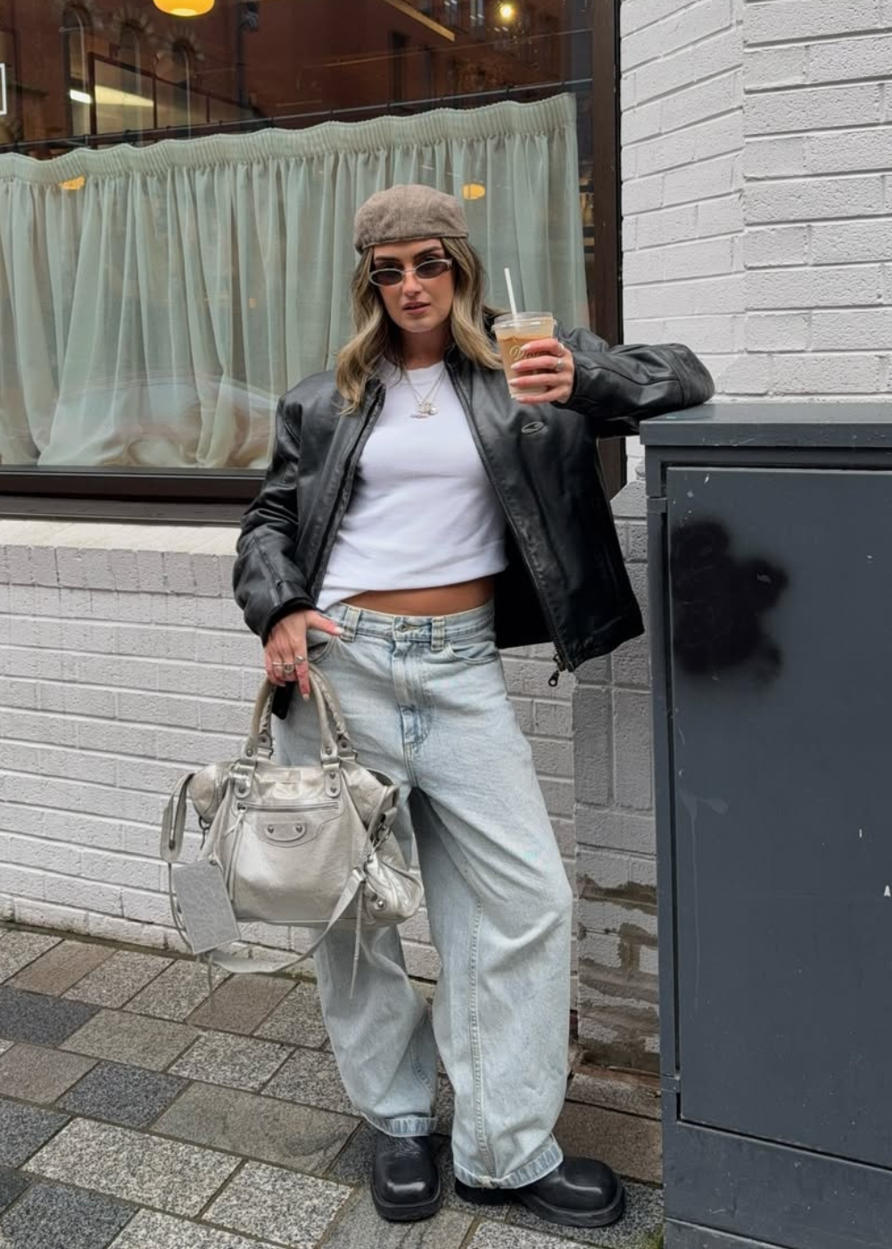 Modelo posa com looks estilosos e confortáveis usando jaqueta preta oversized de couro, camiseta branca cropped e calça jeans