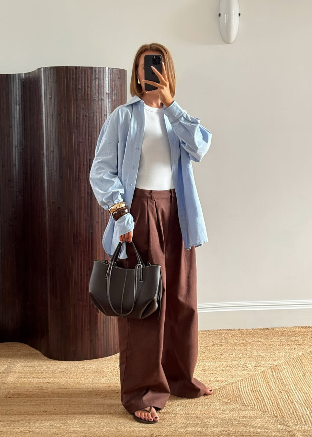 Modelo posa com looks estilosos e confortáveis usando camisa azul oversized, regata branca justa e calça marrom ampla.