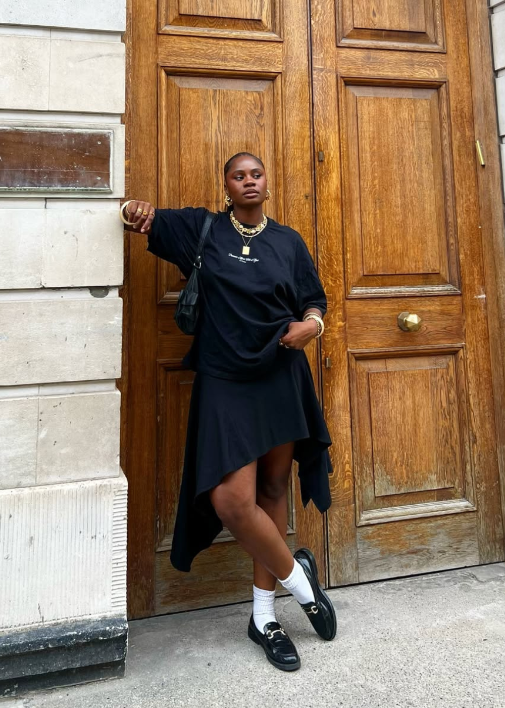 Modelo posa com looks estilosos e confortáveis usando camiseta preta oversized, saia assimétrica e mocassim preto.