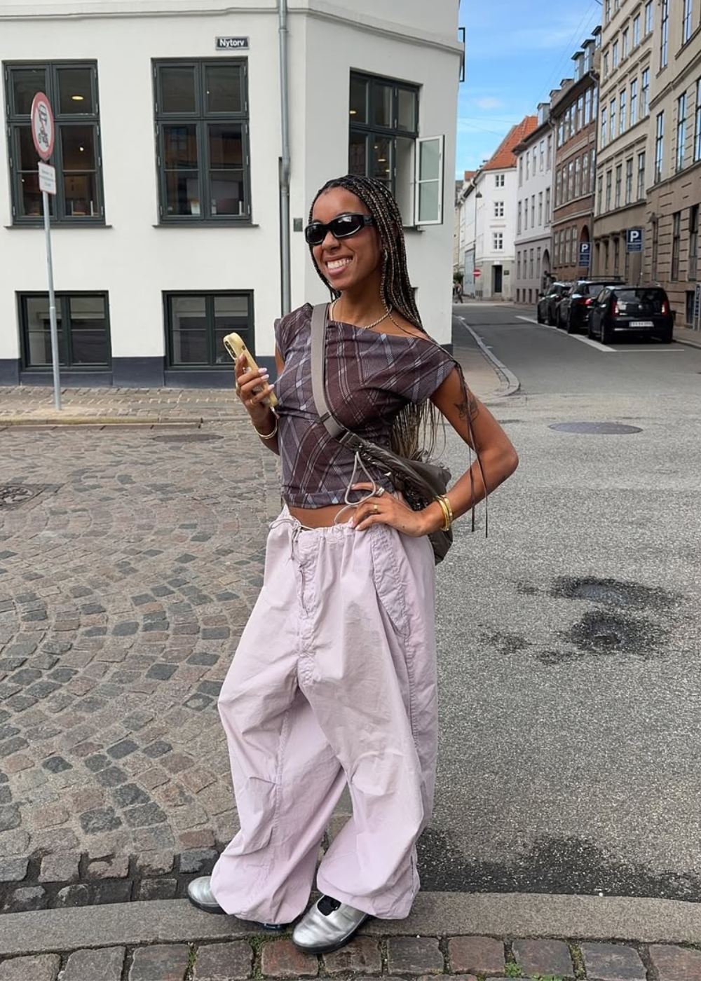 Looks para o Lollapalooza 2026 com top xadrez cropped, calça baggy lilás, tênis prata e acessórios minimalistas.