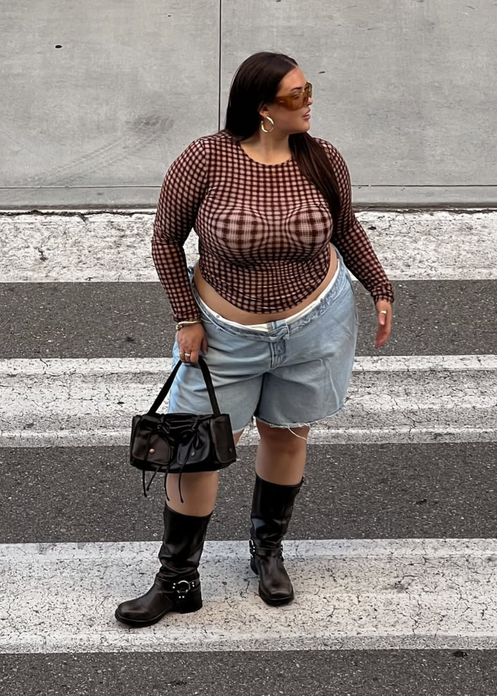 Looks para o Lollapalooza 2026 com blusa cropped xadrez marrom, bermuda jeans clara, botas pretas e bolsa de couro.