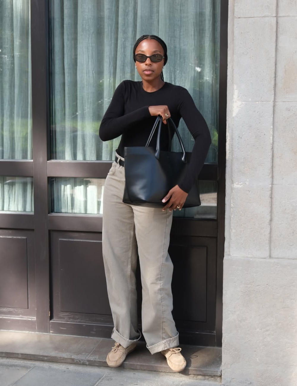 Looks de meia-estação com modelo posa em malha preta ajustada, calça bege reta e bolsa ampla, clima urbano sóbrio.