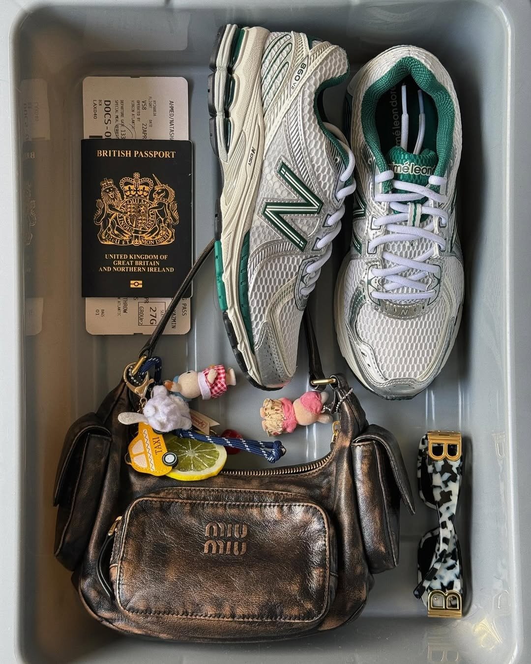 Mala perfeita para viagem a trabalho com tênis branco e verde, bolsa metalizada e passaporte. Texto: BRITISH PASSPORT MIU MIU