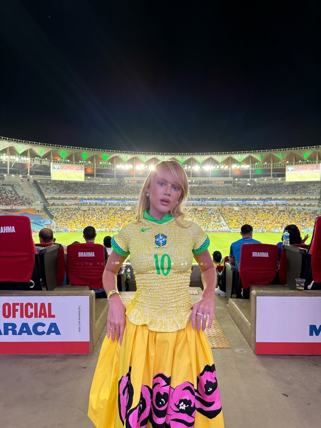 Looks nada óbvios para a copa: modelo posa com camisa amarela franzida e saia ampla floral no estádio Texto: BRAHMA