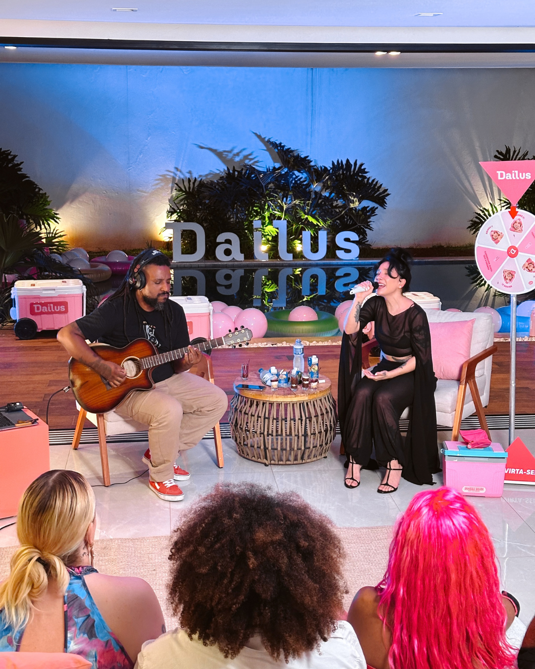 Marketing de experiência em evento Dailus com cantora de vestido preto fluido e violonista casual diante do público.
