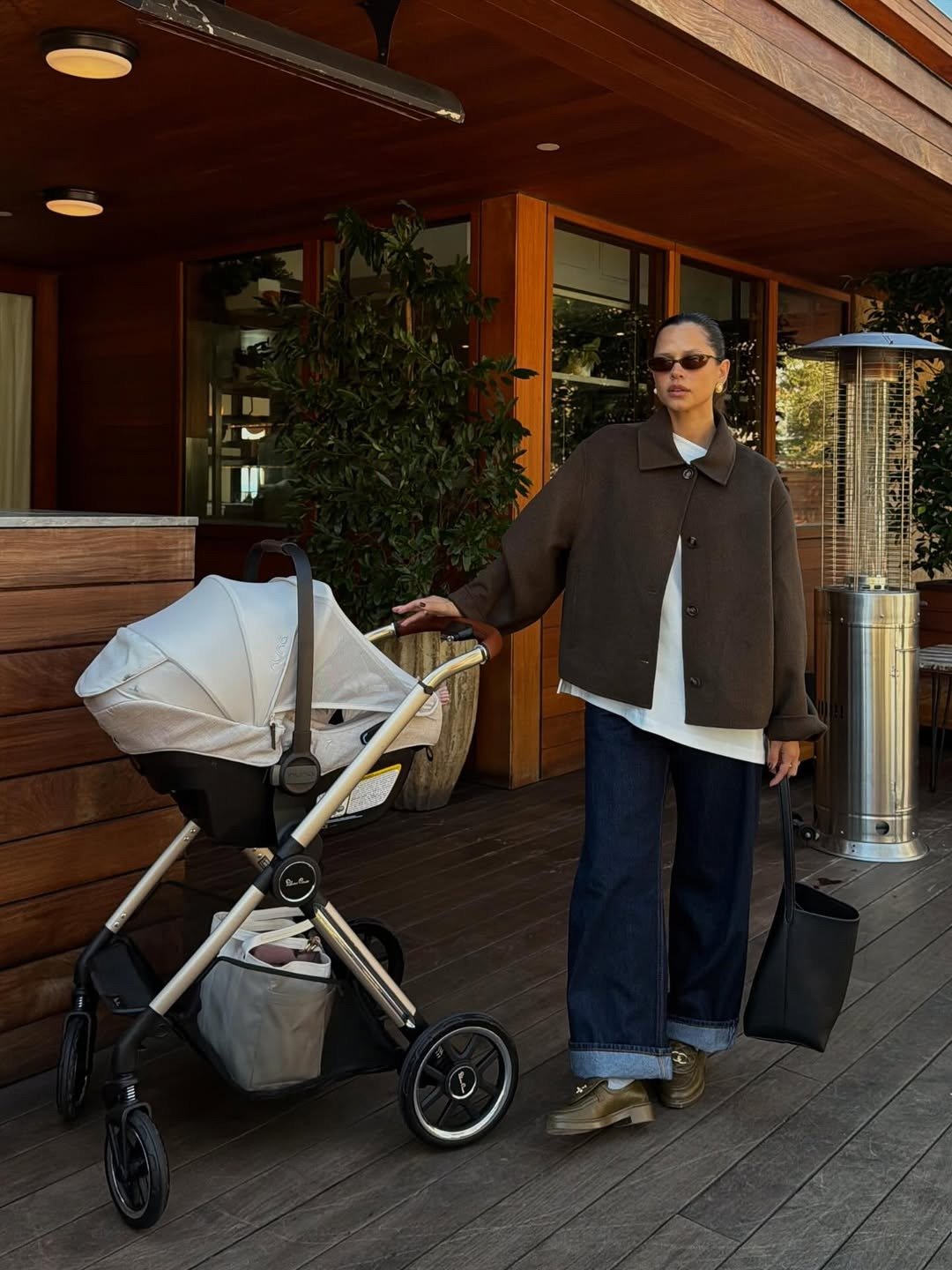 Mocassim feminino com calça jeans ampla; modelo posa com carrinho em look marrom, branco e azul de clima elegante.