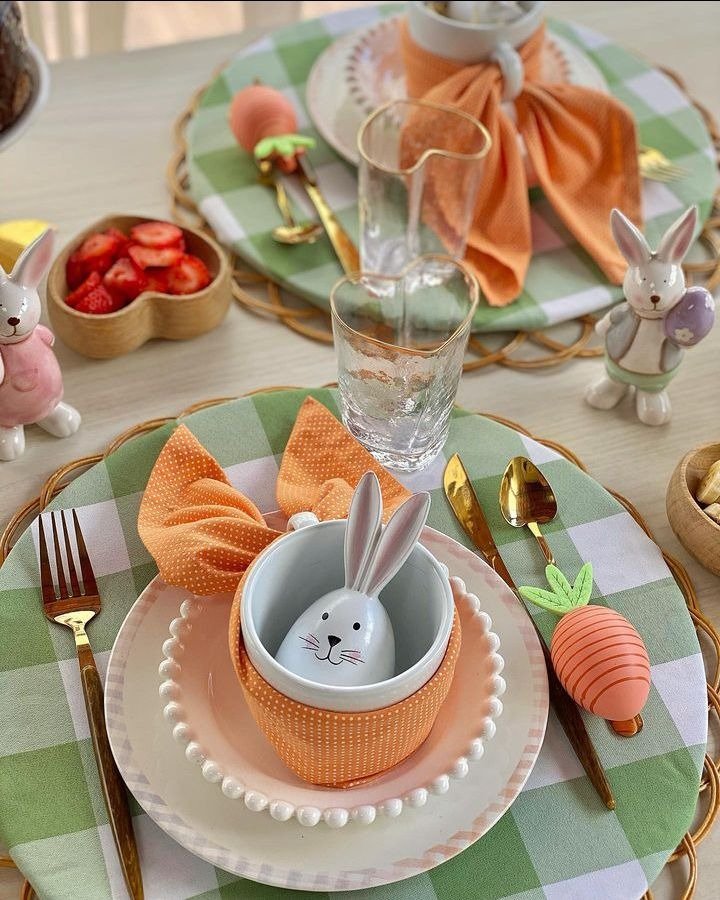 Mesa posta para Páscoa com xadrez verde, louça rosa, guardanapo laço laranja, coelho e talheres dourados delicados
