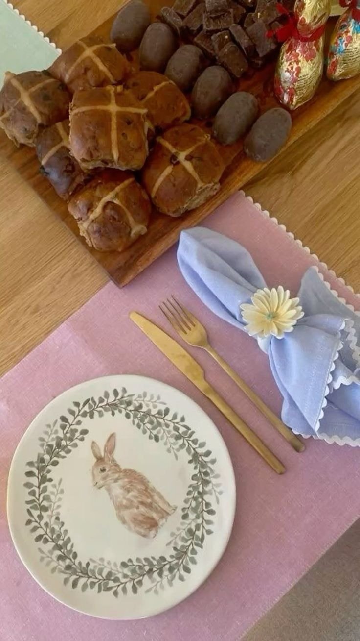 Mesa posta para Páscoa com prato de coelho, guardanapo azul com flor, talheres dourados e pães com chocolates em madeira