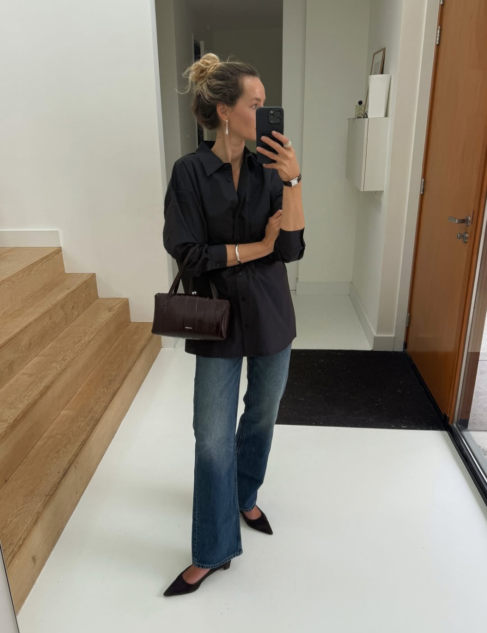 Mulher posa em pé de frente ao espelho. Usa camisa preta e calça jeans boot cut.