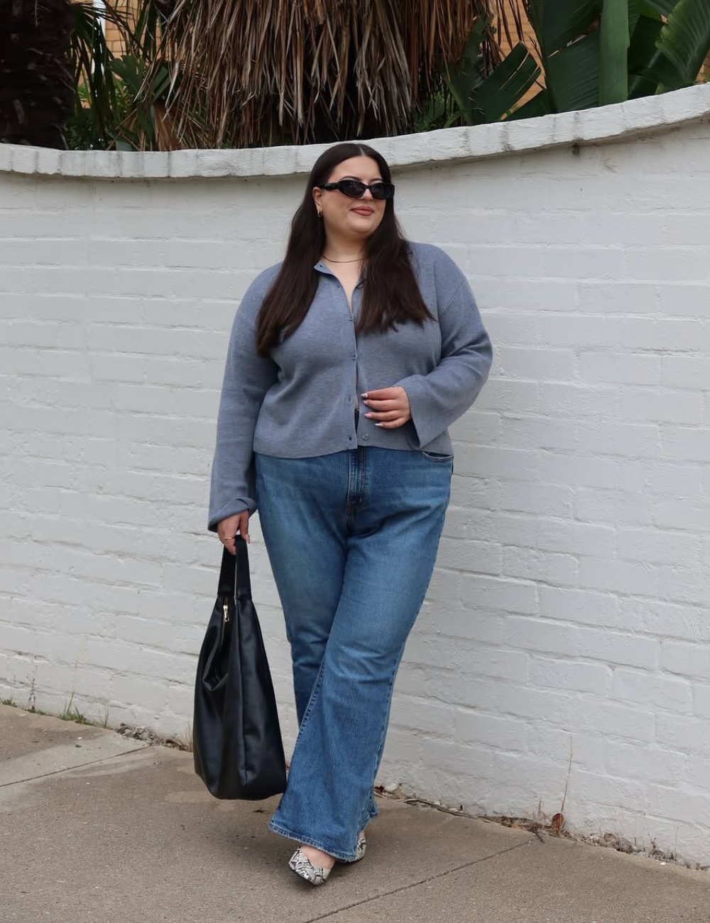 Mulher em pé na rua usando calça jeans feminina boot cut, blusa cinza e sapato com estampa de animal print.