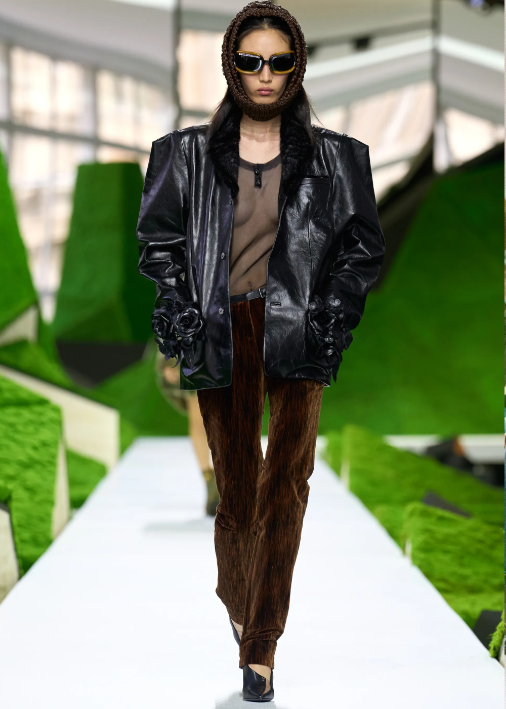 Outono/Inverno 2026: modelo desfila com blazer de couro preto, calça marrom aveludada e clima urbano sofisticado