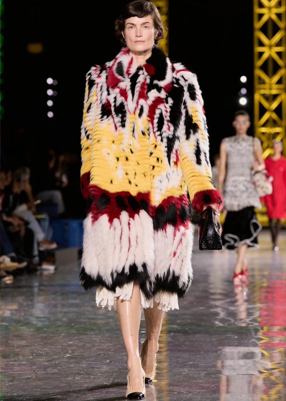 Outono/Inverno 2026: modelo desfila casaco felpudo multicolorido de volume marcante em passarela, com elegância ousada